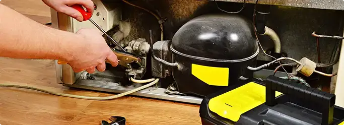 Refrigerator repair technician fixing the compressor and wiring in Gladstone, OR