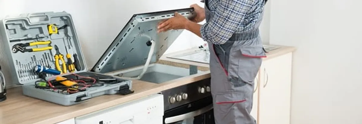 Cooktop repair technician lifting a built-in stovetop for service in Portland, OR