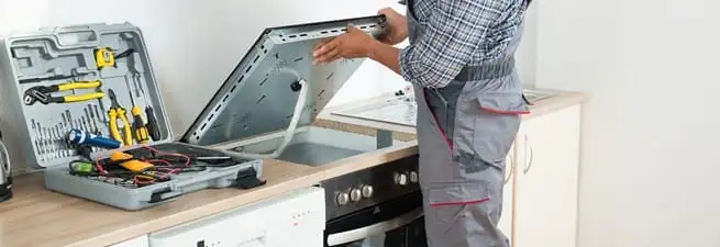 Cooktop repair technician lifting a built-in stovetop for service in Portland, OR