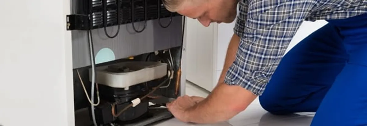 Refrigerator repair technician servicing the compressor and condenser area in Portland, OR