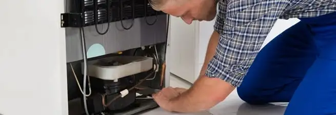 Refrigerator repair technician servicing the compressor and condenser area in Portland, OR