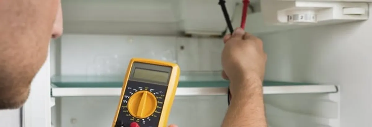 Refrigerator repair technician testing electrical components with a multimeter in Portland, OR
