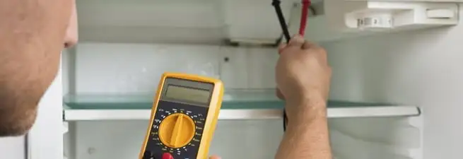 Refrigerator repair technician testing electrical components with a multimeter in Portland, OR