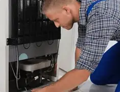 Refrigerator repair technician servicing the compressor and condenser area in Portland, OR